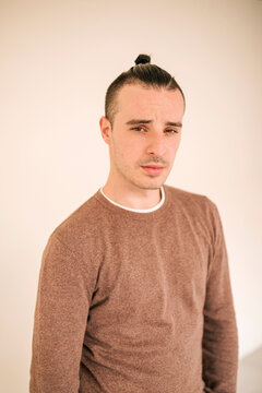 Young gay man in brown t-shirt standing against beige background
