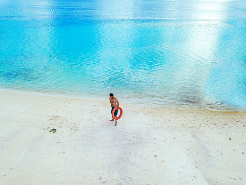 Shirtless man holding inflatable ring looking away while standing on shore at beach