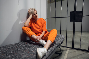 Girl convicted drug dealer in an orange jumpsuit in his cell on a prison bunk.