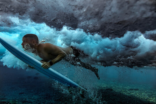 Male surfer duck diving in water with surfboard at Maldives