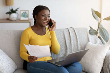 Black Freelancer Lady Talking On Cellphone And Working With Papers At Home