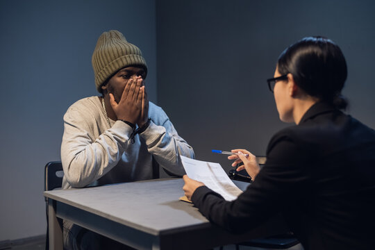 A young girl lawyer consults her client at the police station, a black guy in a cap and handcuffs