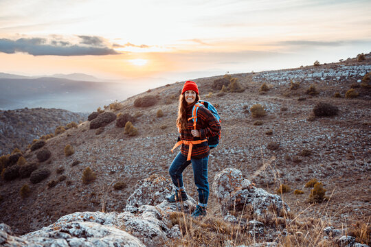 Smiling female hiker looking away while standing on rock mountain during sunset