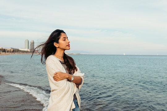 Young woman with arms crossed standing on water against sky at beach