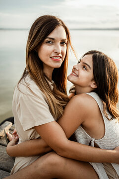 Mother and daughter embracing each other at jetty against lake