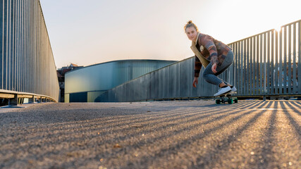 Carefree young woman skateboarding on footbridge against clear sky at sunset