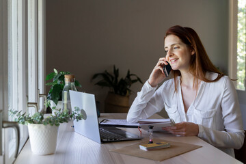 Smiling doctor talking on mobile phone while working on laptop at home