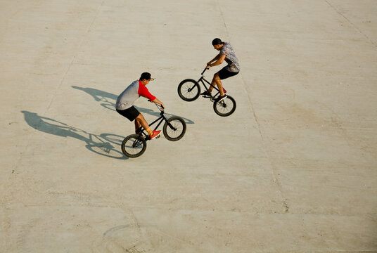 Young men doing wheelie stunts on footpath during sunny day