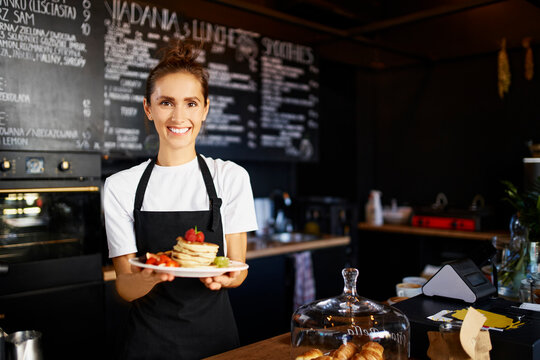 Portrait of smiling female barista giving pancakes in plate at cafe