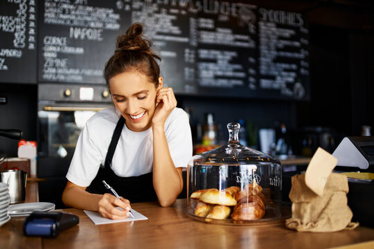 Smiling barista writing in note pad while working at cafe