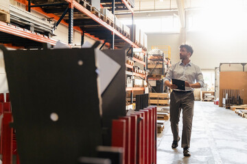 Businessman with digital tablet inspecting warehouse while standing at factory
