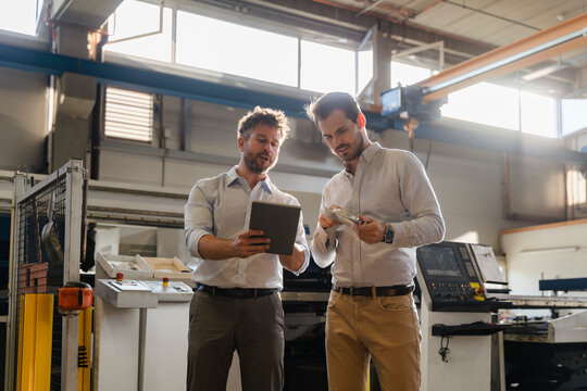 Businessmen using digital tablet while examining metal object at factory