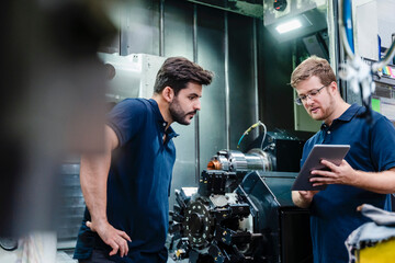 Male coworkers discussing while using digital tablet in manufacturing factory