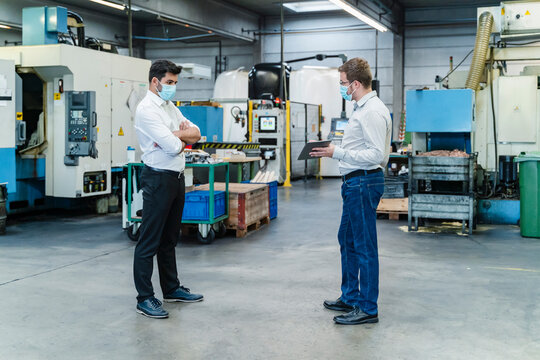 Male coworkers discussing while maintaining social distancing in factory