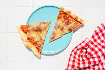 Two slices of pizza Margherita on blue plate and red checkered napkin