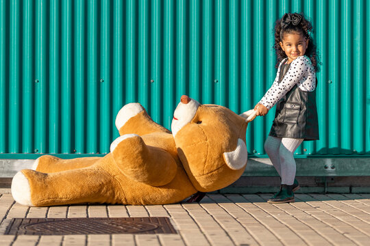 Girl dragging teddy bear on footpath while standing against green wall