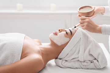 Asian woman getting skin treatment at spa, beautician applying clay face mask