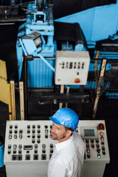 Male owner looking away while standing control panel in factory