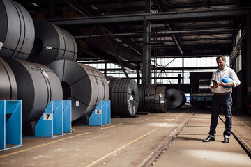 Businessman text messaging on smart phone while standing in factory