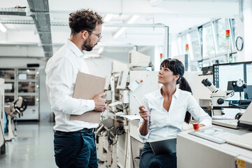 Confident female technician discussing with male colleague at laboratory