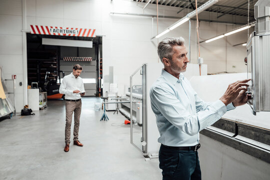 Businessman operating machinery while colleague standing in background at factory