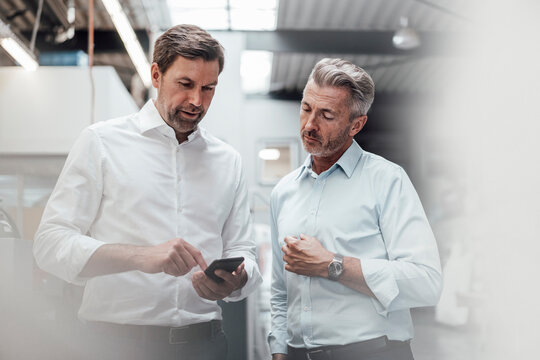 Mature businessmen discussing over smart phone while standing in industry