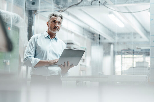 Contemplating male engineer with laptop looking away while standing in industry