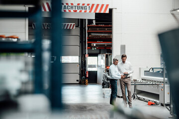 Male engineers discussing over digital tablet while standing in factory