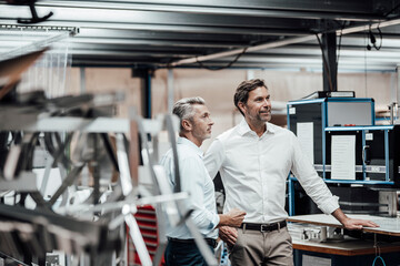 Mature colleague discussing with smiling manager while standing by manufacturing machinery in factory