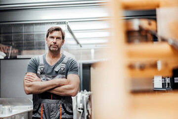 Confident mature male worker standing with arms crossed in factory
