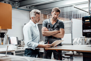 Mature manager discussing with worker over document while standing in factory