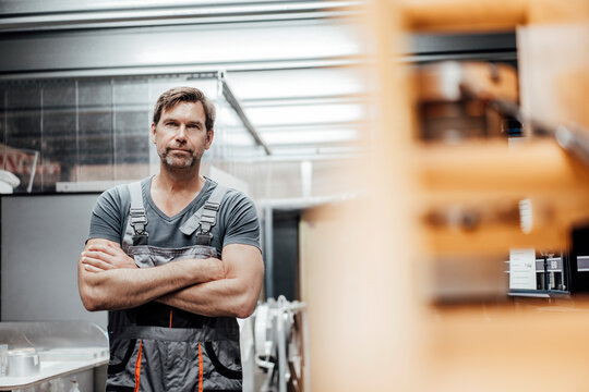 Confident mature male worker standing with arms crossed in factory