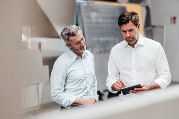 Mature businessmen discussing over digital tablet while standing in industry