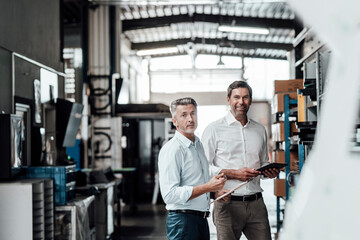 Smiling engineers with digital tablet standing in manufacturing industry