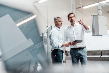 Male engineer with digital tablet pointing while discussing with colleague in manufacturing industry