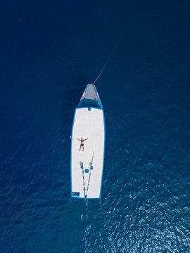 Aerial view of shirtless man relaxing on roof of boat drifting in blue waters of Arabian Sea in summer