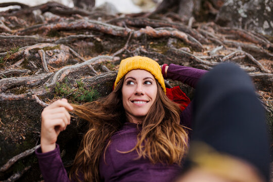 Smiling woman looking away while lying on tree roots in forest at La Pedriza, Madrid, Spain
