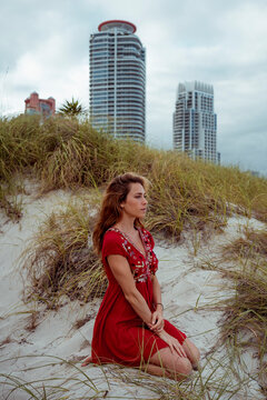 Young woman looking away while kneeling on sand at beach
