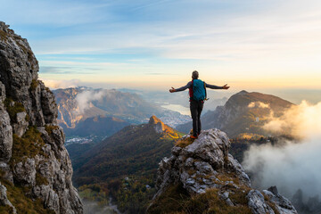 Pensive hiker with arms outstretched standing on mountain during sunrise at Bergamasque Alps, Italy