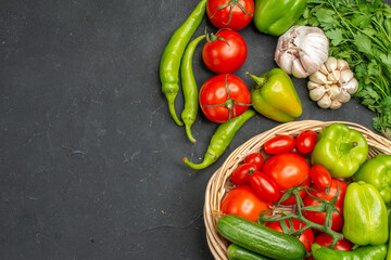 Above view of fresh various organic vegetables inside and outside of a wicker basket on the left side on dark background