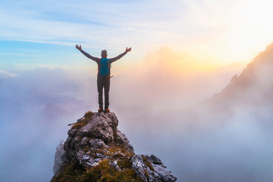 Pensive male hiker with arms outstretched standing on mountain peak during sunrise at Bergamasque Alps, Italy