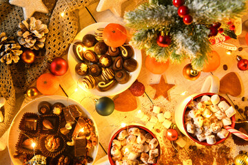 sweet food top view background for merry christmas or new year holiday decoration with night illumination - chocolate candies, tangerines, cookies, marshmallow and cocoa latte on white wood