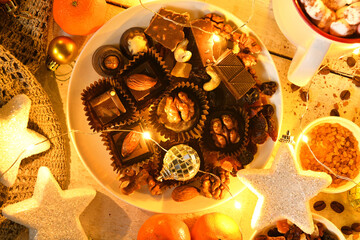 sweet food top view background for merry christmas or new year holiday decoration with night illumination - chocolate candies, tangerines, cookies, marshmallow and cocoa latte on white wood