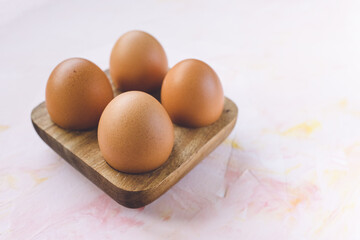 Four brown eggs in a wooden storage organizer box on pink background. Useful household items, organic healthy bio product and Easter holiday concept. Close up, copy space