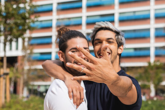 Smiling man showing engagement ring while standing by gay partner in park