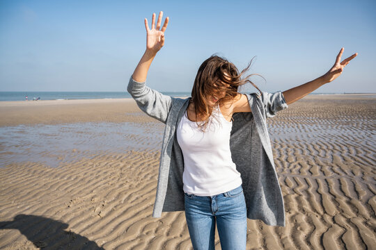 Happy young woman dancing at beach against clear sky during sunny day
