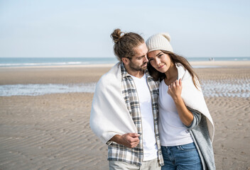 Young couple covered in blanket spending leisure time at beach during weekend