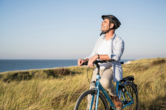 Smiling man with eyes closed sitting on bicycle at beach against clear sky