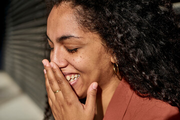 Young woman laughing with eyes closed against shutter on sunny day