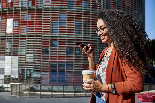 Smiling woman sending voicemail through smart phone while standing in city during sunny day